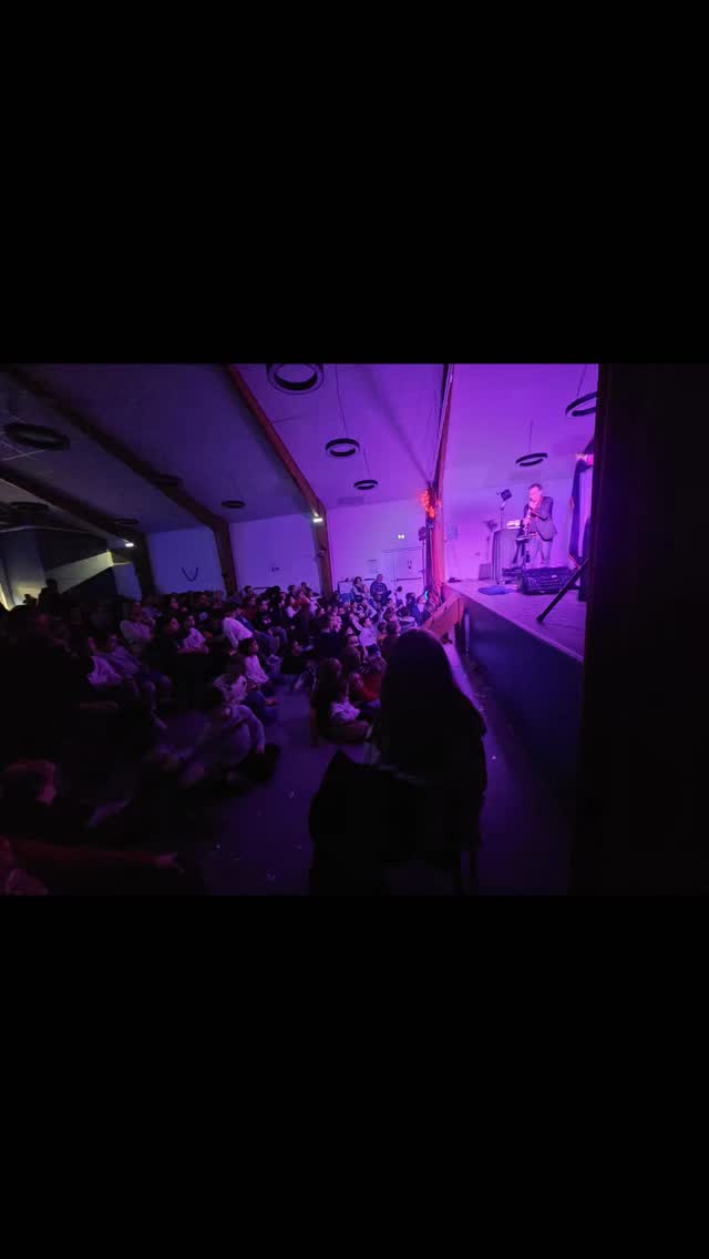 Vue de côté d’une salle de spectacle avec le public face à Magie Sam sur scène.
