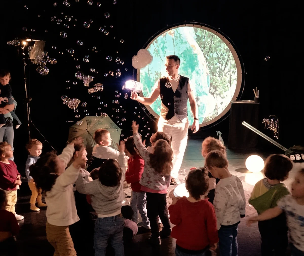 Magie Sam fait voler des bulles devant des enfants qui participent au spectacle.